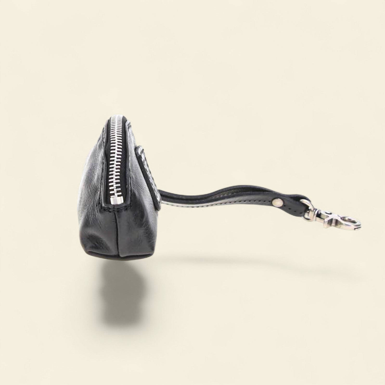 Black leather coin purse with a visible brand logo on a beige background