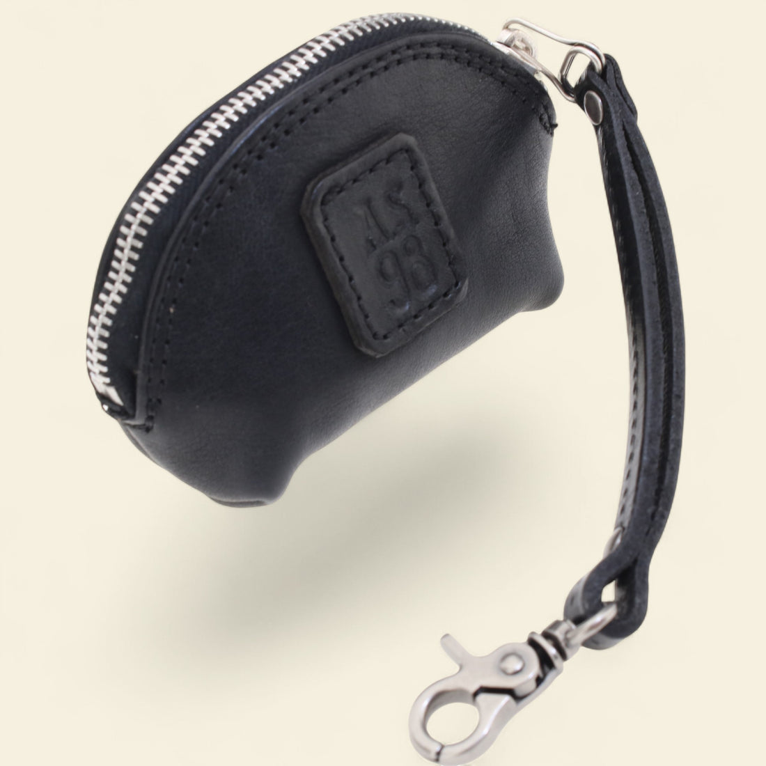 Black leather coin purse with a visible brand logo on a beige background 